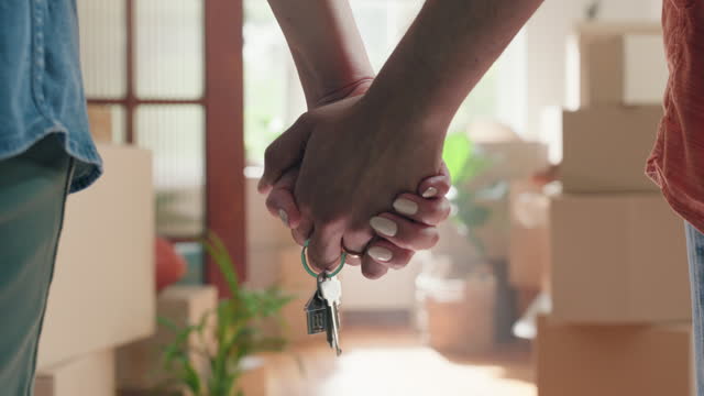 Couple, keys and holding hands in new home, moving and boxes for relocation, real estate or property investment. Man, woman and together with beginning, growth and future with cardboard in lounge