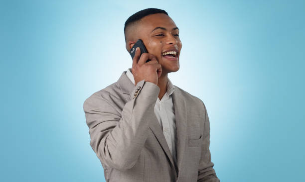 istock Business man, phone call and laugh in studio for consulting, communication and chat on blue background. Happy worker, mobile networking and contact for feedback, conversation and funny discussion 1855219403