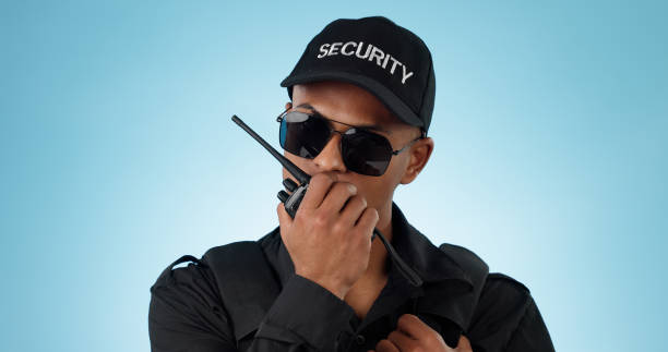 istock Security, radio and an officer man on a blue background in studio for surveillance or communication. Face, uniform and sunglasses with a young law person speaking on a walkie talkie for patrol 1855232933