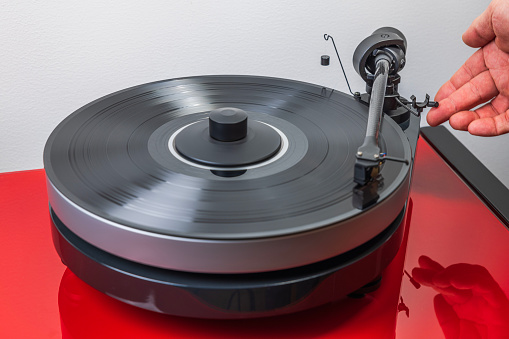 In a close-up, a person sets a vinyl player in motion, gently lowering the tonearm onto the vinyl record.