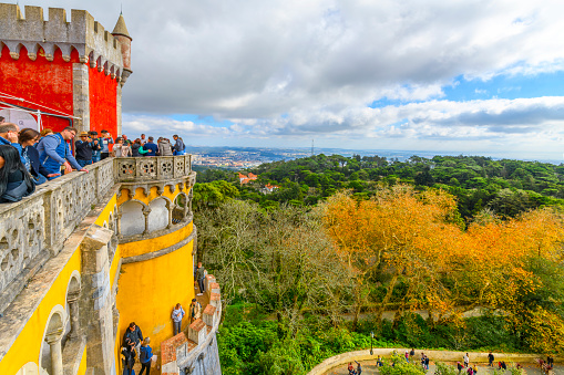 The effects of overtourism are visible as tourists pack all the levels and terraces on a crowded autumn day at the National Palace of Pena, a colorful, touristic 19th century castle in the Sintra Mountains above the town of Sintra, Portugal, close to the capital city of Lisbon on the Portuguese Riviera.