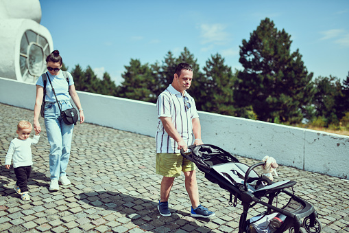 Male With Down Syndrome Pushing Baby Stroller Of Family While Mother Walks With Toddler