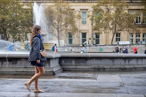 Trafalgar Square, London, England - October 30th 2023:  Young woman walking in front of one of the famous fountains