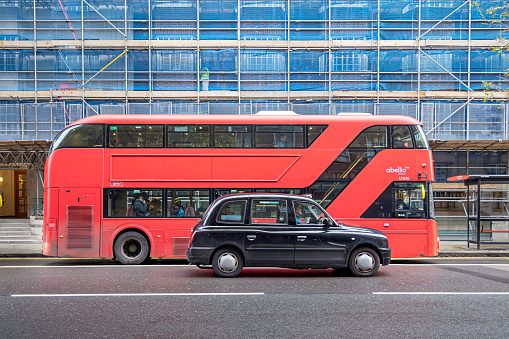 Woburn Place, London, England - October 30th 2023: Red London double-decker bus and taxi in front of a scaffolding with blue tarpaulin
