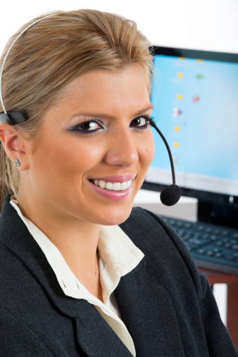 Woman in business suit talking on a headset, looking at camera smiling.
