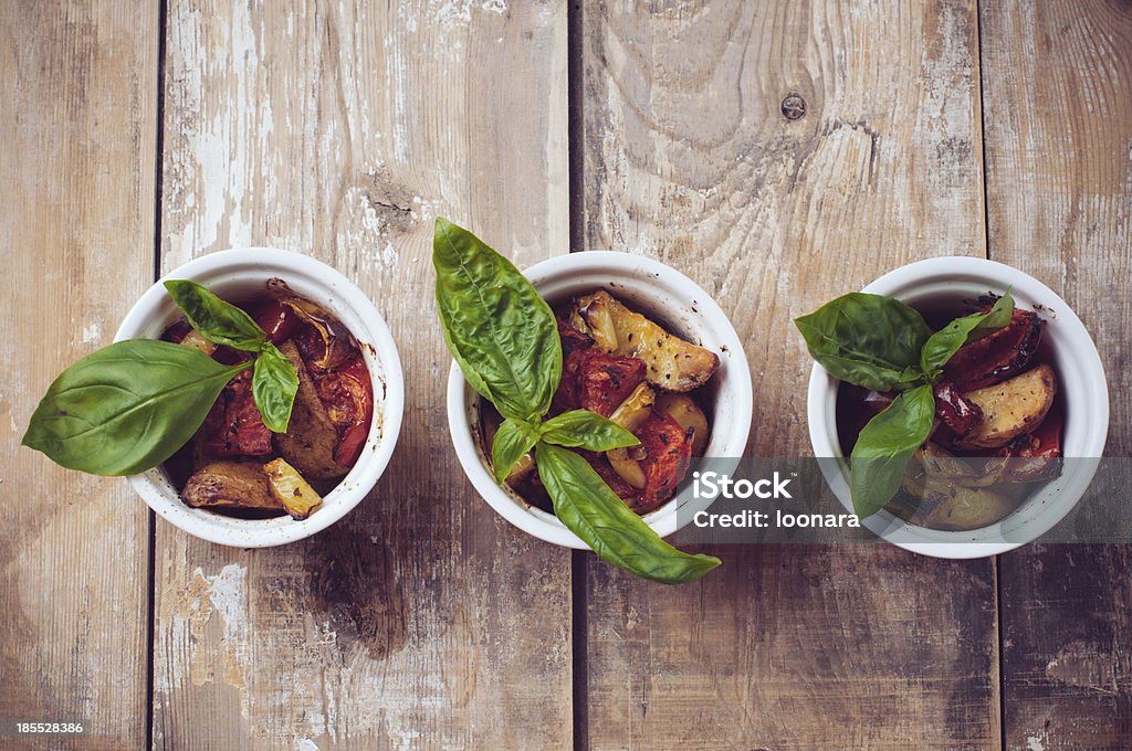 Vegan food: three plates of grilled vegetables Vegan homemade food: three plates of grilled vegetables, tomatoes, potatoes and peppers with basil on a wooden board Arrangement Stock Photo