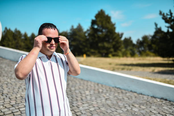 Front View Of Male With Intellectual Disability Putting On Sunglasses While Walking In Park