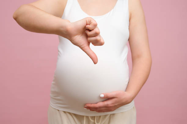 istock Pregnant woman showing thumbs down gesture, studio pink background 1855309552