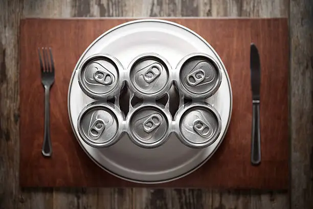Conceptual image representing alcoholism on a funny way using a six-pack of beer cans for dinner.
