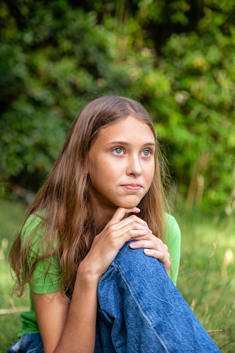 Young girls using jeans and green shirt sitting in the grass in the park