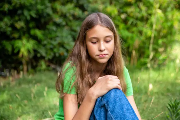 Young girls using jeans and green shirt sitting in the grass in the park