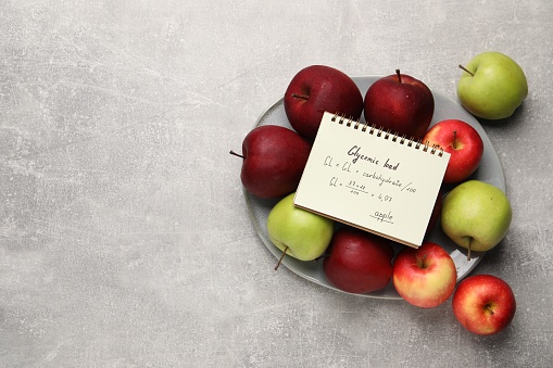Notebook with calculated glycemic load for apples and fresh fruits on light grey textured table, top view. Space for text