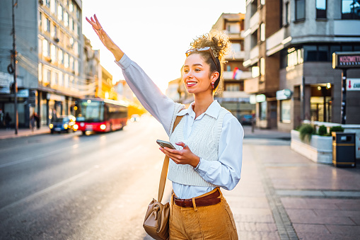 Young beautiful smiling woman waving to catch a taxi in the city