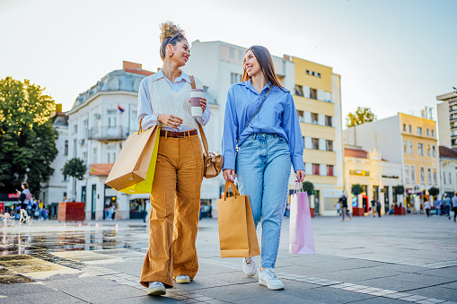 Cheerful young female friends walking together in the city  after a successful shopping spree