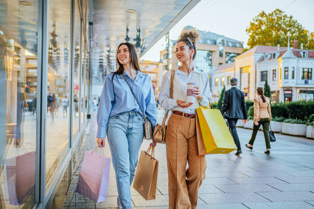 Female friends looking at store window Young cheerful female friends looking at store windows while shopping together in the city boutique stock pictures, royalty-free photos & images