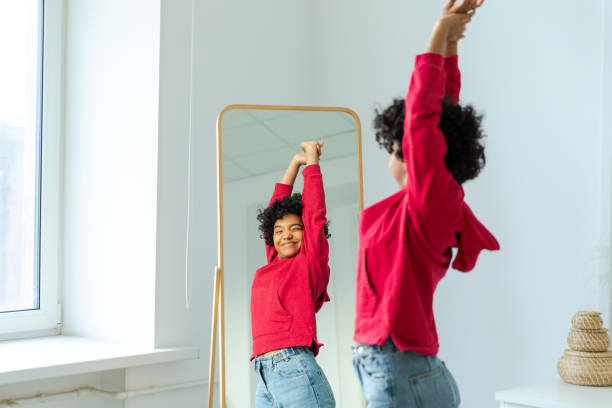 istock Love yourself. Beautiful young smiling african american woman dancing enjoying her mirror reflection. Black lady looking at mirror looking confident and happy. Self love concept. 1855407607