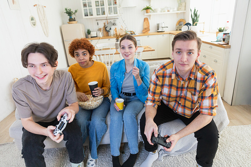 Home party. Cheerful group of friends playing video games at home. Happy diverse group buddies having fun together indoor. Friendship leisure entertainment concept. Young best friends enjoying weekend