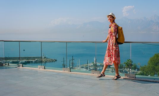 female summer travel to Antalya, Turkey. young asian woman in red dress walk through old town Kalechi , Panoramic view of Antalya Old Town port, Taurus mountains and Mediterrranean Sea, Turkey