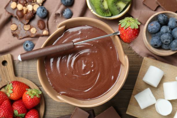 istock Fondue pot with melted chocolate, marshmallows, fresh kiwi, different berries and fork on wooden table, flat lay 1855453748