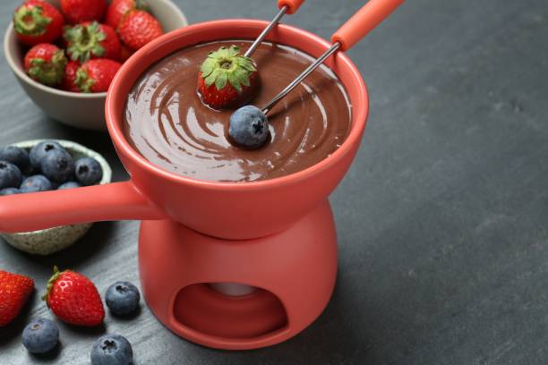istock Dipping fresh berries into fondue pot with melted chocolate at grey table, closeup. Space for text 1855453788