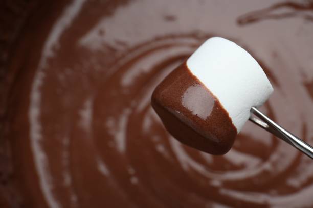 istock Marshmallow with melted chocolate on fork above fondue, closeup. Space for text 1855455389