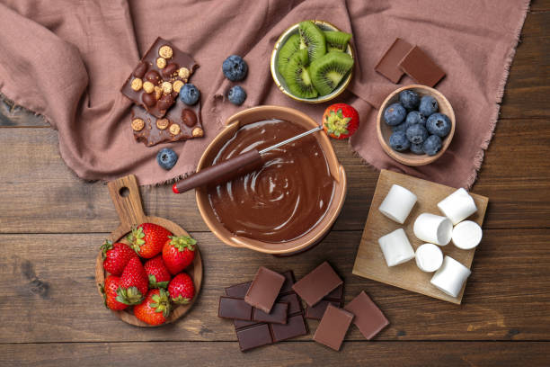 istock Fondue pot with melted chocolate, marshmallows, fresh kiwi, different berries and fork on wooden table, flat lay 1855455391