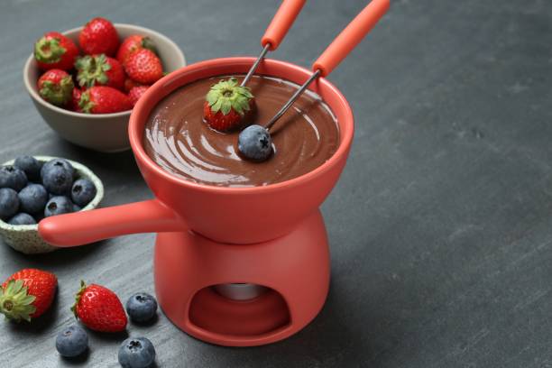 istock Dipping fresh berries into fondue pot with melted chocolate at grey table. Space for text 1855457486