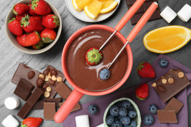 istock Fondue pot with melted chocolate, fresh orange, marshmallows and different berries on grey table, flat lay 1855459060
