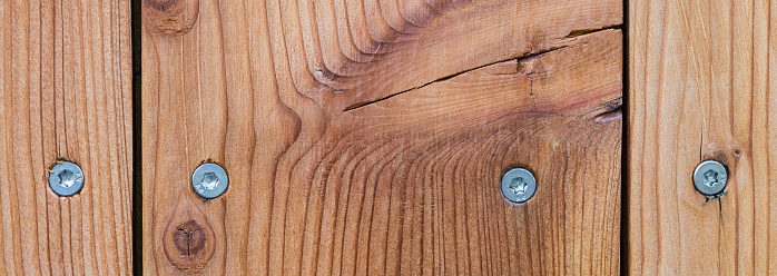 Paneling detail of natural planks with narrow slits, a crack and stainless self-drilling torx woodscrews in brown texture. Woodwork