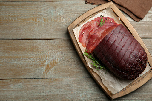Tasty bresaola, peppercorns and rosemary on wooden table, top view. Space for text