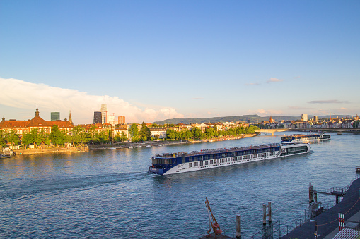 Basel, Switzerland - May, 16. 2022: River tourist cruises on the Rhine River through Basel Stadt in the sunset time.