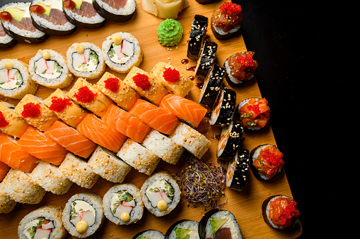 Close up macro color image depicting a delicious arrangement of fresh traditional Japanese sushi rolls topped with smoked salmon, prawn and avocado. There is a dish filled with soy sauce and also wooden chopsticks.