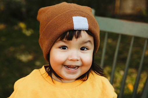 An image of a Native American two~year~old girl smiling as she sits on a chair outside.