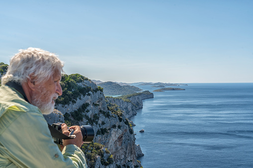 Man, rear view, photographing the view of cliffs of Telascica, national park in Dugi otok island, Kornati islands in background. Croatia