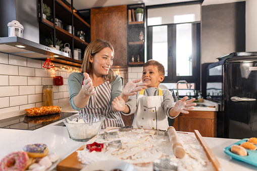 Photo of a cheerful mother and son playing with dough while preparing sweets in the kitchen - Togetherness and bonding