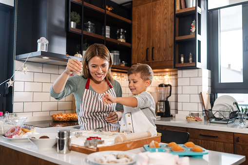 A mid-adult woman is starting her small business with cookies. Her little son is helping her. They are in the kitchen surrounded by various sweets - Hobbies and leisure activities