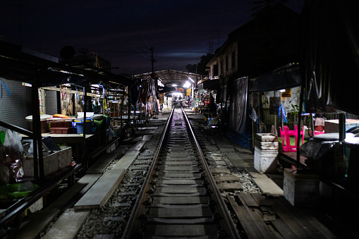 Tracks passing past the shops and stores at night. The Rom Hub Market is famous for an active railroad passing directly through the busy outdoor market space in Mae Klong, Thailand