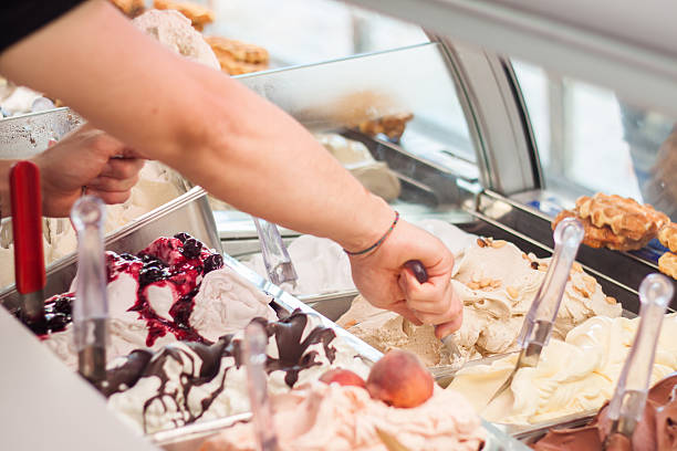Close-up of a variety of ice cream flavors in a gelateria This is a photo of a man who sell ice-cream in ice-cream shop Italian gelateria. The man is filling waffle with an ice cream with his hand. The display case inside with ice creams is seen in the background. display cabinet photos stock pictures, royalty-free photos & images