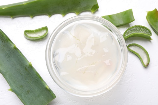 Aloe vera gel and slices of plant on white background, flat lay