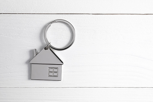 Metal keychain in shape of house on white wooden table, top view. Space for text