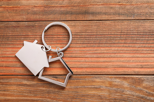 key with a small wooden house in hand against the background of the silhouette of a door and a fence on the site