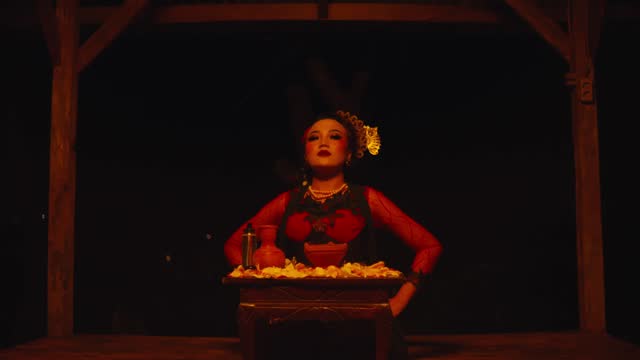an Asian woman is sitting in front of the ritual offerings with a sly and scary expression