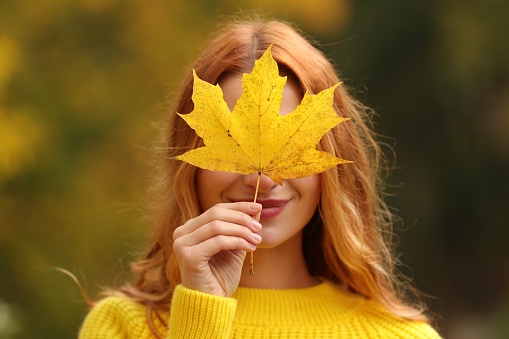 Woman covering face with autumn leaf outdoors