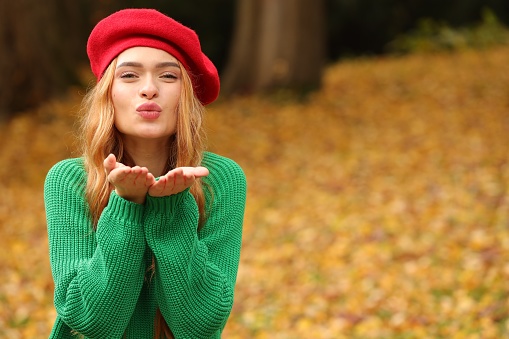 Portrait of beautiful woman blowing kiss in autumn park. Space for text