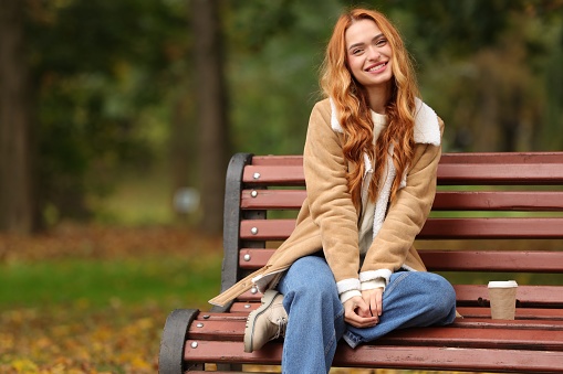 Portrait of smiling woman sitting on bench in autumn park. Space for text