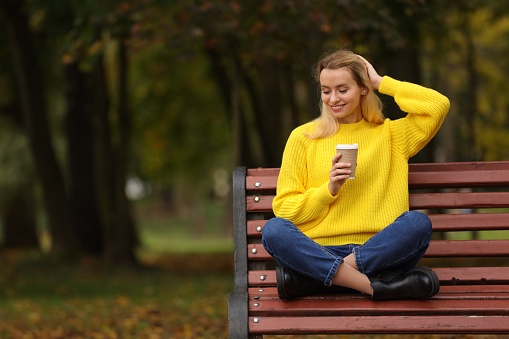 Happy woman with paper cup in autumn park. Space for text