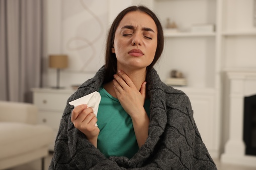 Sick woman wrapped in blanket with tissue at home. Cold symptoms