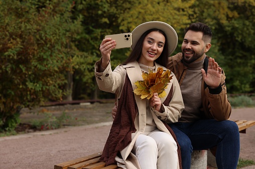 Happy young couple taking selfie in autumn park, space for text