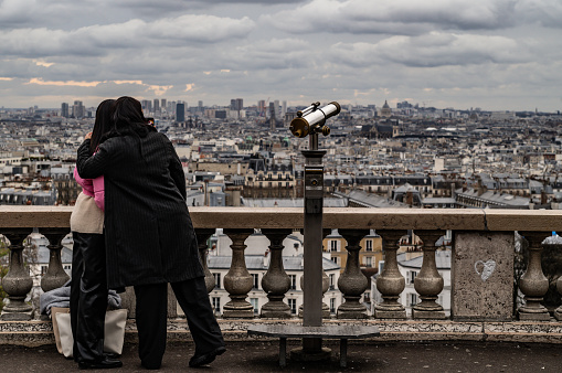 A couple or women stands in front of a view of Paris from Montmartre district, on December 14, 2023.