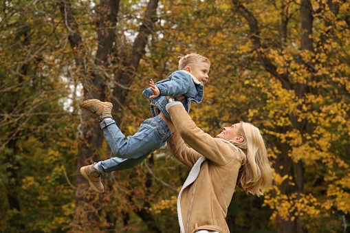 Happy mother playing with her son in autumn park, low angle view